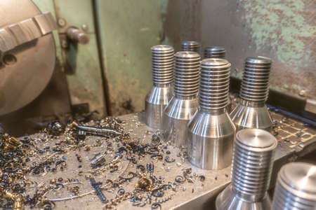 Bolt threading on a lathe in a machine shop, finished products on a machine bed.