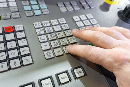 The worker switches the buttons on the remote control of the CNC machine, the control of the...