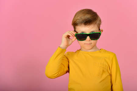 Glamorous and stylish boy posing for the camera, model in sunglasses, in yellow clothes in the studio on a pink background.の写真素材