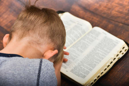 The child prays over the open book of the Bible, the boy folded his arms and bowed in peace in prayer to God.の写真素材