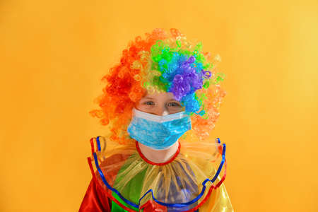 Sad and sad baby clown in a protective medical mask from coronavirus on a yellow background.