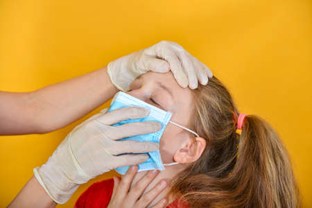 A doctor in medical gloves examines a girl in a protective mask for signs of coronavirus.の写真素材