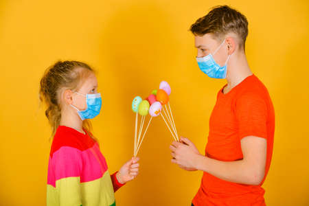 A boy with a girl in a protective mask from a coronavirus give each other Easter eggs on a holiday.の写真素材