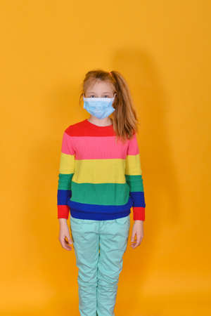 Girl standing in a protective mask on a yellow background. Children and personal protective equipment....の写真素材