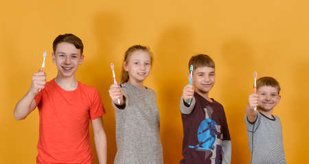 Children hold a toothbrush in their hands and stand in a row on a yellow background