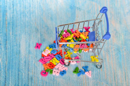 Colored letters of the English alphabet on a trolley, consumer basket with the alphabet on a blue...