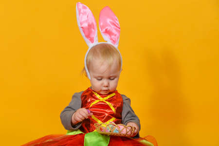 A small child, a girl clown with rabbit ears holds Easter eggs in her hands