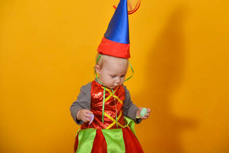 A small child, a girl in a clown hat, holds Easter eggs in his handsの写真素材