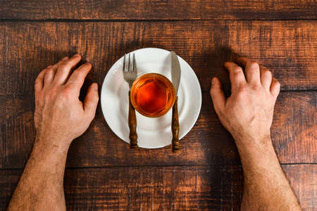 A man copes with alcohol addiction, cognac on a plate with a fork and knife.