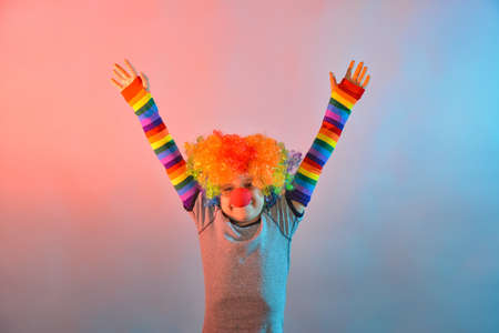 Joyful boy in a clown wig and with a red nose holds his hands to the sides.の写真素材