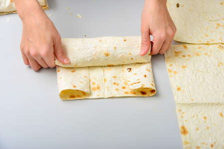 Woman cook rolls up fried meat and salad in pita, cooking shawarmaの写真素材
