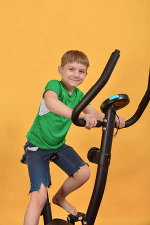 The boy goes in for sports, the child on a stationary bike does cardio and looks forward to the camera.の写真素材
