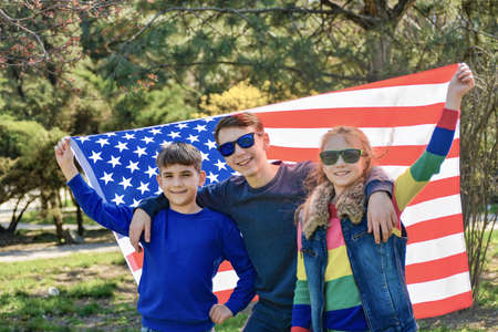 Three teenage children stand together and hold the American flag behind.の写真素材