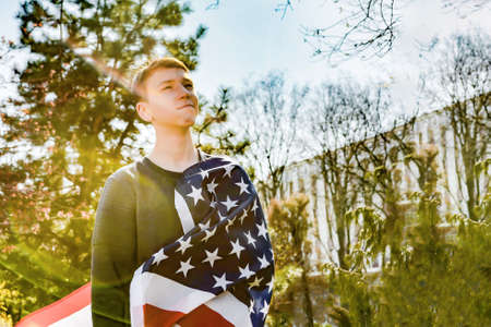 A teenager patriot, holds the American flag on his chest and looks away, as a symbol of US victory and patriotism.の写真素材