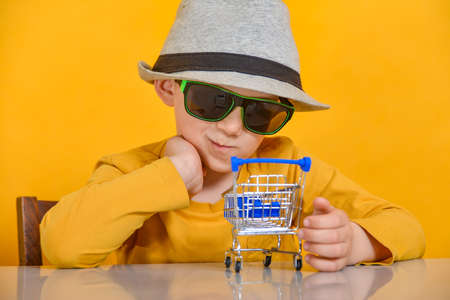 A boy in a hat and sunglasses looks at the shopping cart, the concept of choice and preparation for shopping in storesの写真素材