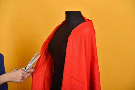 A woman cuts a red cloth with scissors, reconciling on a black mannequin.