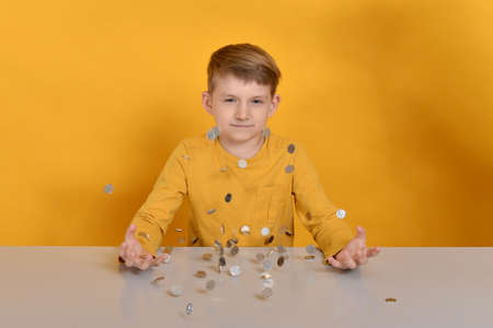 Silver coins are falling on the table to the child in an orange T-shirt.の写真素材