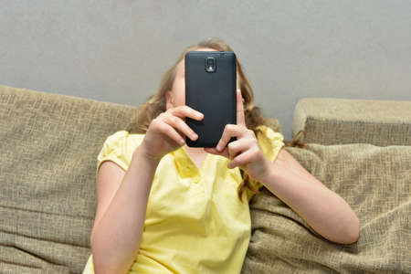 A woman is sitting with a phone on a sofa at home.