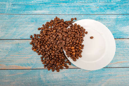 Roasted coffee grains are scattered on a plate on a blue wooden backgroundの写真素材