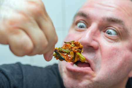 A crazy man with bulging eyes looks at fatty and junk food, sending it into his mouth. The concept of obesity and eating.の写真素材