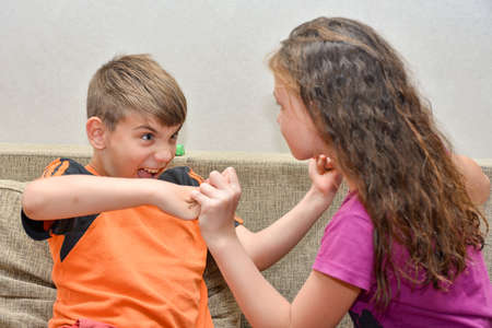 Angry boy fights with a girl at home on the couch, brother and sister quarrel