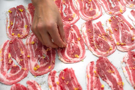 Woman housewife pickles thinly sliced bacon slices with garlic and spices on the table. Cooking junk...
