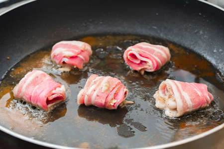 Raw rolls with bacon are fried in a pan. Cooking junk and fatty foodsの写真素材