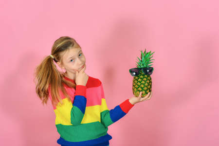 A girl in a striped sweater is looking at a pineapple with glasses.の写真素材