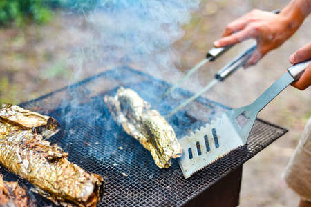 The cook fries the fish on the net and turns it over on the fire. Outdoor BBQ weekendの写真素材
