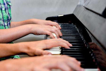 Brother and sister play the piano with four hands. Children learn the art of music