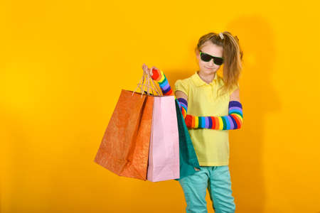 A girl with glasses stands with packages and poses on an orange background.の写真素材