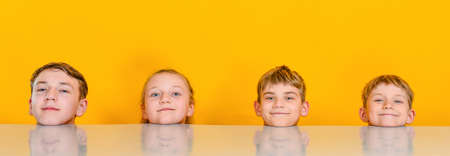 Children are sitting at the table, only their heads are visible. Widescreen concept photoの写真素材