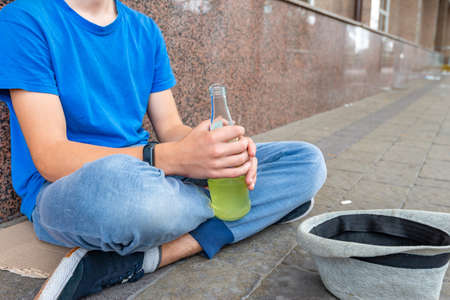 A teenager with alcohol in his hands sits on the street and begs.の写真素材