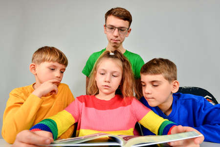 Three brothers and a sister thoughtfully read a book.の写真素材