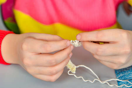 A girl sits at a table and tries to learn how to knit herself.