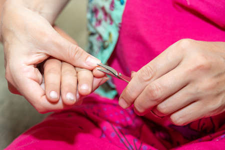 Mom holds her baby's hand and trims her nails with small baby scissors. Care and guardianship of children by parentsの写真素材