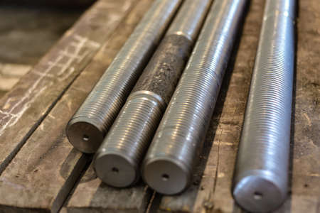 After turning and milling, the threaded studs lie on a wooden rack in the warehouse
