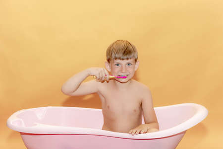 A small child brushes his teeth while sitting in the bathroom, on a yellow background.の写真素材