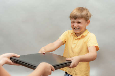 A naughty boy, addicted to computer games, snatches a laptop out of his parents' hands.の写真素材