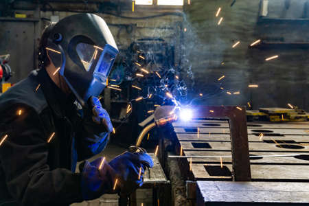 An electric and gas welder in an electromechanical workshop welds a metal structure at a mechanical...