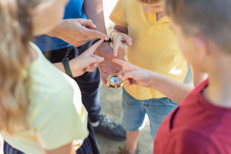 Four children look at the compass and point their fingers in different directions.の写真素材