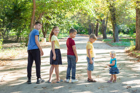 Five children stand in a row in height in the park, walking and relaxing in nature.