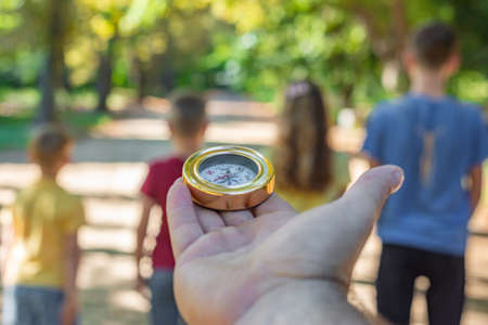 A man's hand with a compass, children are standing in front of him and waiting for directions of movementの写真素材