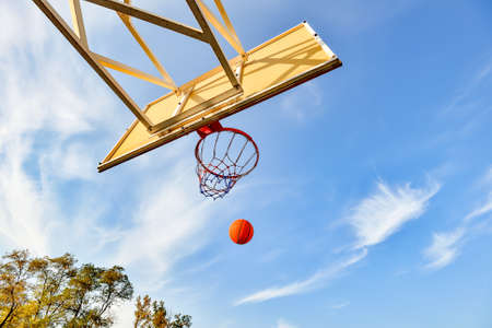 Flying basketball ball in the hoop on the background of the cloudy sky. Sports activities on the...