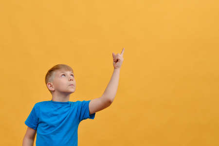 Surprised boy on a yellow background shows thumbs up and looks to the side.の写真素材