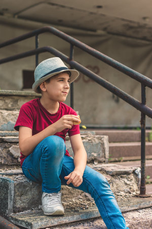 A boy with a hat eats on the steps and looks away.の写真素材