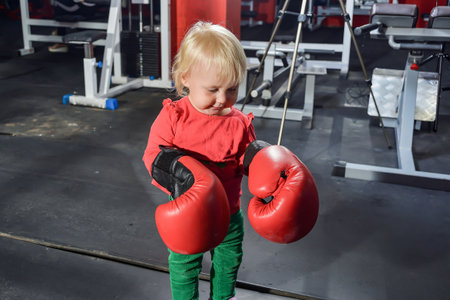 Little girl stands with boxing gloves in the gym.の写真素材