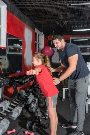 The coach works with the girl in the gym and shows how to do the exercise correctly.