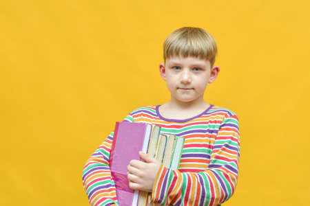 A boy on a yellow background holds a pack of textbooks in his hands