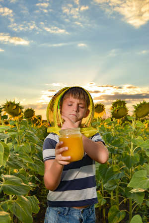 A young beekeeper holds a jar of honey in his hands in a sunflower field.の写真素材